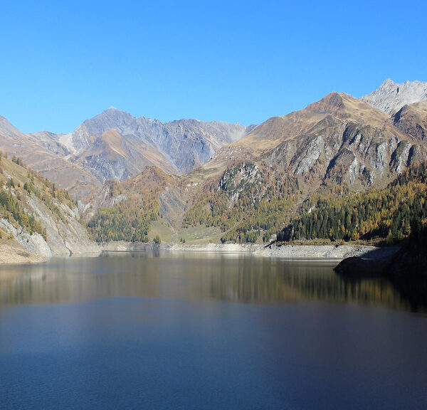 Lago di Luzzone: Ruhiger Bergsee mit Spiegelung der Alpenlandschaft unter blauem Himmel.