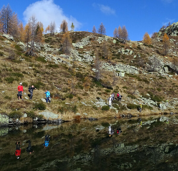 Wanderer am Lago di Mognola spiegeln sich im ruhigen Wasser des Bergsees.