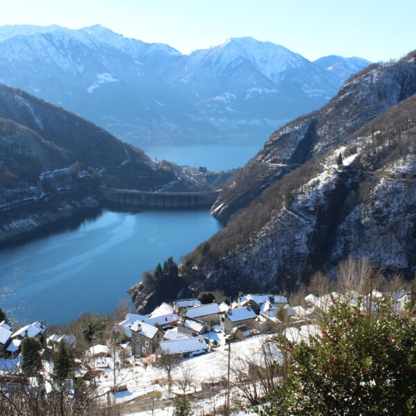 Lago di Vogorno im Winter: Verschneite Häuser am See, Berge im Hintergrund.