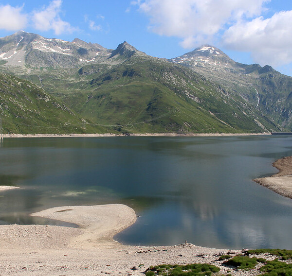 Lai da Sontga Maria: Bergsee mit grünen Hängen und schneebedeckten Gipfeln unter blauem Himmel.