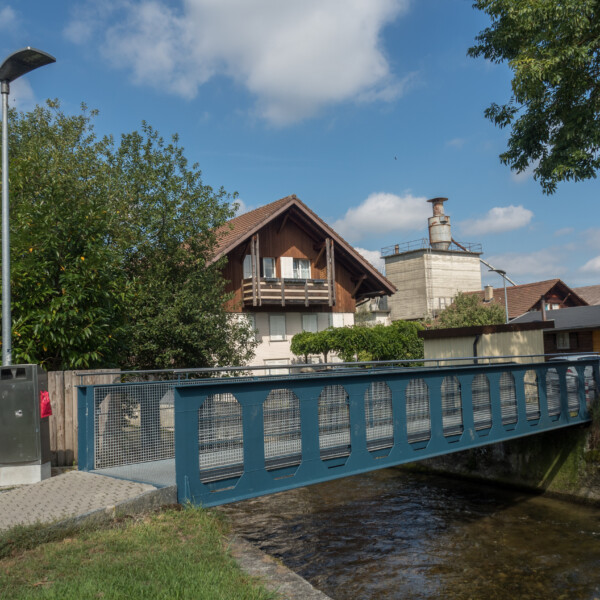 Brücke über die Langeten in der Schweiz mit Haus und Industriegebäude im Hintergrund.