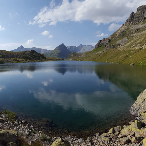 Grevasalvas: Bergsee mit Spiegelung der umliegenden Gipfel unter blauem Himmel.