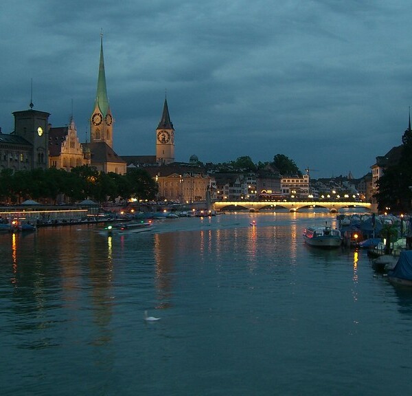 Limmat Fluss Zürich bei Nacht mit beleuchteten Gebäuden und Brücke.