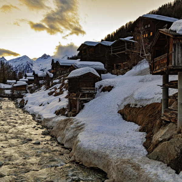 Winterliche Landschaft mit Lonza Fluss und verschneiten Häusern in den Schweizer Alpen.