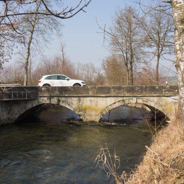 Weißes Auto fährt über eine Steinbrücke über die Lorze.