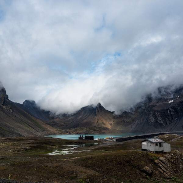 Muttsee unter bewölktem Himmel, umrahmt von Bergen. Landschaft mit Wasser und Gebäuden.