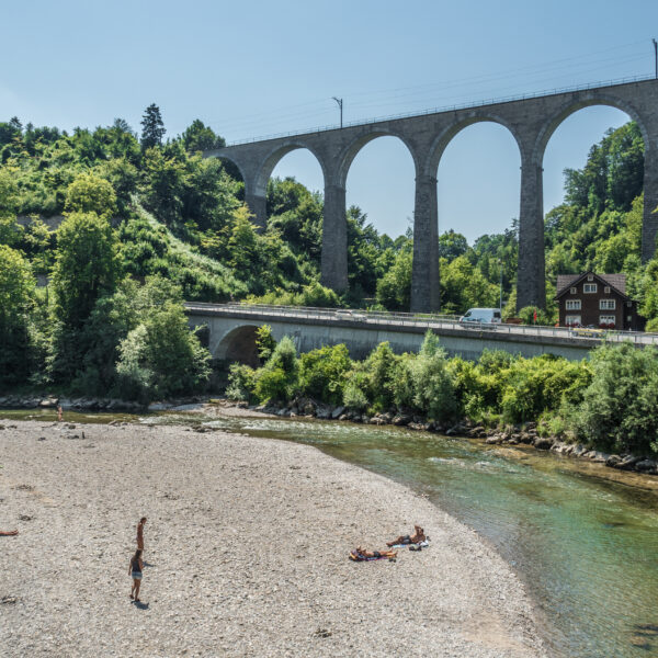 Fluss Necker unter Eisenbahnviadukt und Straßenbrücke, sonnige Landschaft.