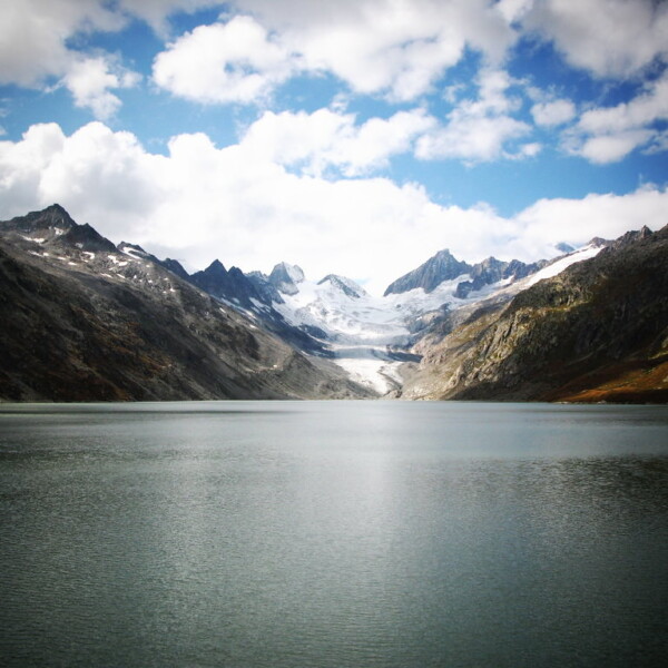 Oberaarsee mit Gletscher und Bergen unter blauem Himmel mit Wolken.