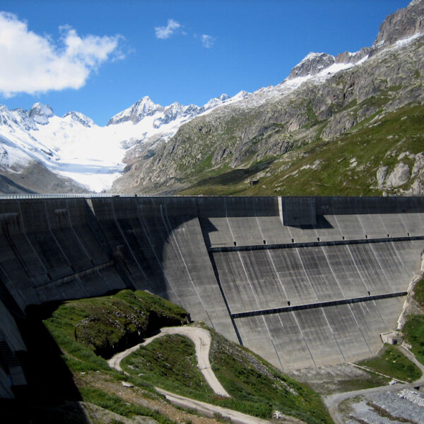 Oberaarsee Staumauer vor schneebedeckten Bergen unter blauem Himmel.