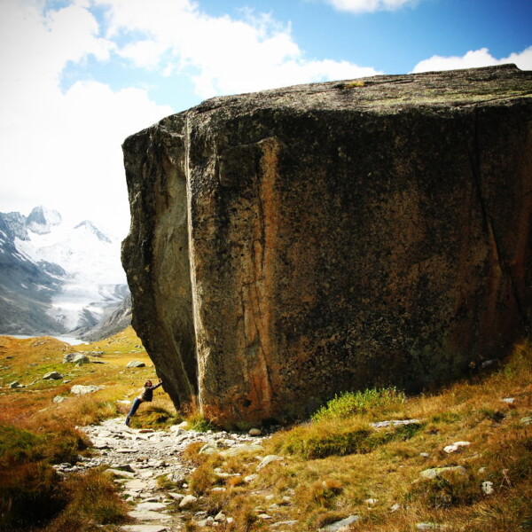 Großer Felsblock am Oberaarsee mit Berglandschaft im Hintergrund.