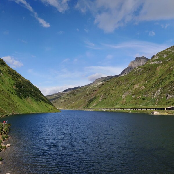 Oberalpsee mit grünen Bergen und blauem Himmel.