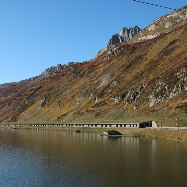 Oberalpsee mit Bergkulisse und Straße. Spiegelung im ruhigen Wasser.