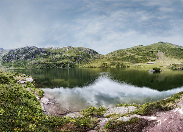 Oberer Murgsee: Ruhiger Bergsee mit Spiegelung des Himmels und grünen Bergen.