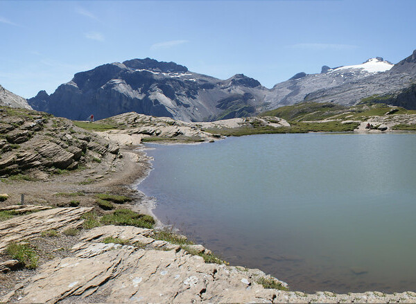 Bergsee Plan des Roses in den französischen Alpen mit Wanderer am Ufer und schneebedeckten Gipfeln.