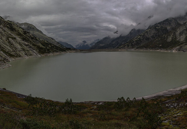Räterichsbodensee-Stausee unter bewölktem Himmel, umgeben von Bergen.