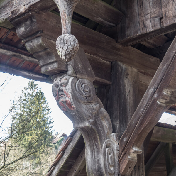 Holzgeschnitzte Figur am Rotbach (Rothenburg) mit Gesicht und Ornamenten.
