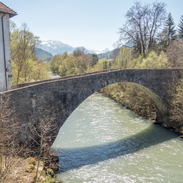 Alte Steinbrücke über die Saane mit Bergen im Hintergrund.