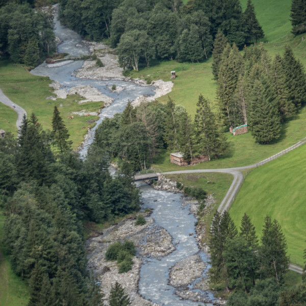 Fluss schlängelt sich durch das Schächen Tal, umgeben von grünen Wiesen und Bäumen.