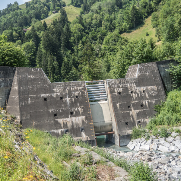 Betonsperre im Schächen-Tal, umgeben von grüner Natur und einem klaren Bachlauf.