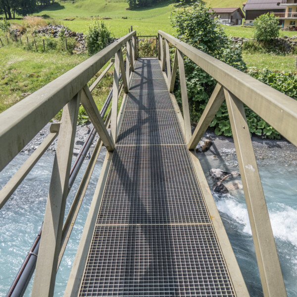 Metallbrücke über türkisfarbenen Fluss in Schächen. Landschaft mit grünen Wiesen.