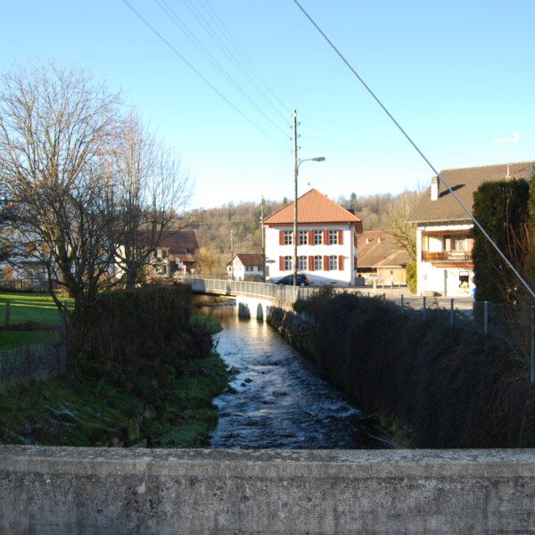 Scheulte: Dorfansicht mit Bach, Brücke und Häusern im Schweizer Jura.