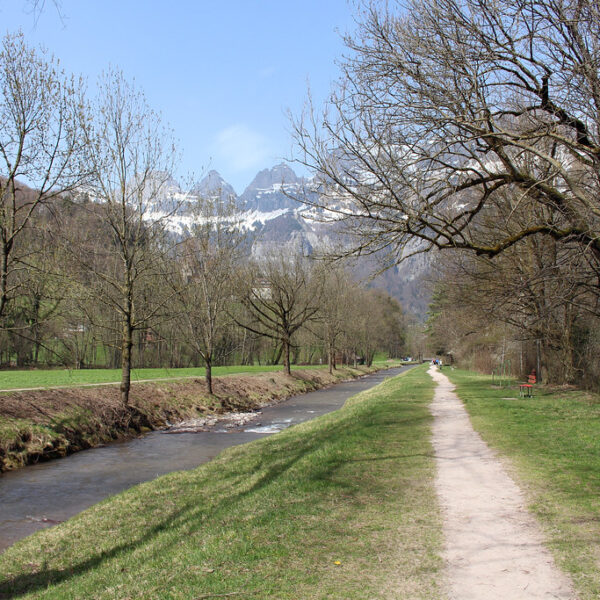 Schils-Fluss mit Wanderweg und schneebedeckten Bergen im Hintergrund.