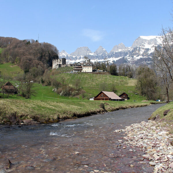 Schils Landschaft mit Fluss, Burg und schneebedeckten Bergen im Hintergrund.