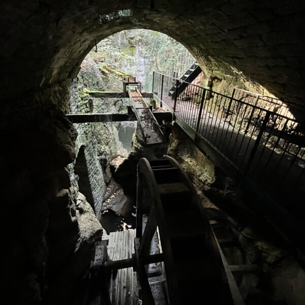 Seyon: Wasserrad in dunkler Schlucht mit Steg und Felswänden.