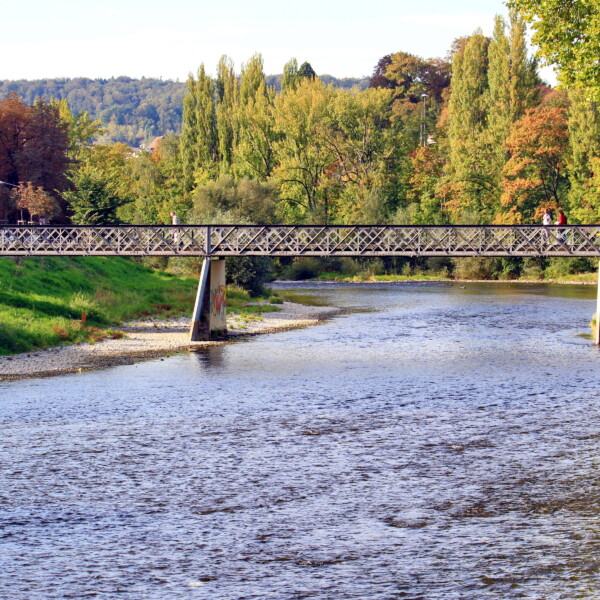 Fußgängerbrücke über die Sihl im Herbst. Bäume mit bunten Blättern im Hintergrund.