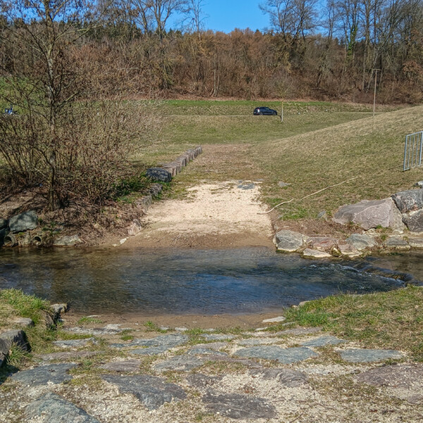 Bachlauf mit Steinen und Sandweg im Grünen. Surb könnte in der Nähe sein.