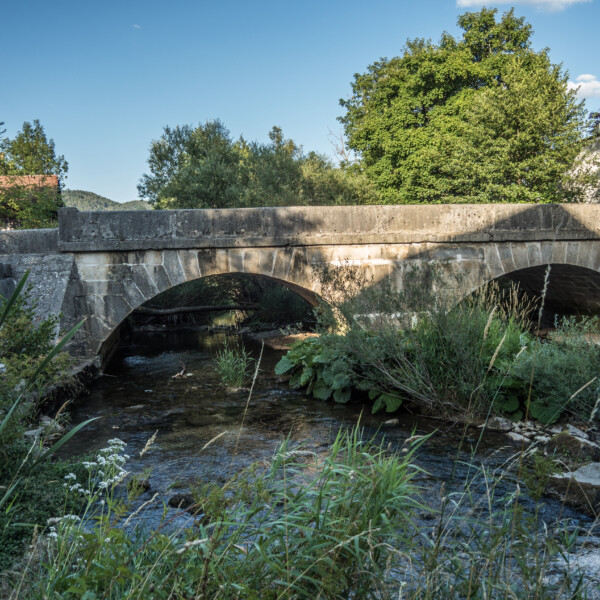 Steinbrücke über die Suze (Schüss) mit Person am Ufer. Ländliche Szene in der Schweiz.