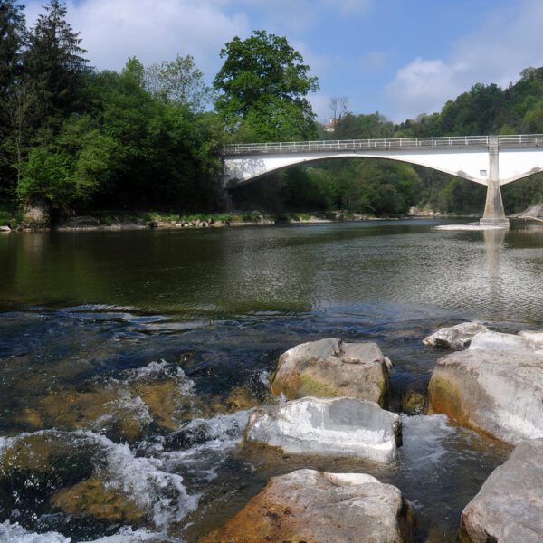 Fluss Thur unter einer weißen Bogenbrücke, umgeben von grüner Natur und Felsen.