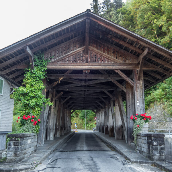 Gedeckte Holzbrücke in Trueb, Schweiz mit Blumen und grüner Vegetation.