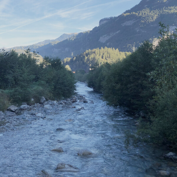 Ürbachwasser-Fluss mit Bäumen und Bergen im Hintergrund.