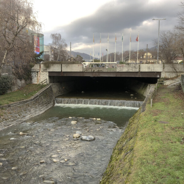 Fluss Veveyse unter einer Brücke mit Flaggen im Hintergrund.