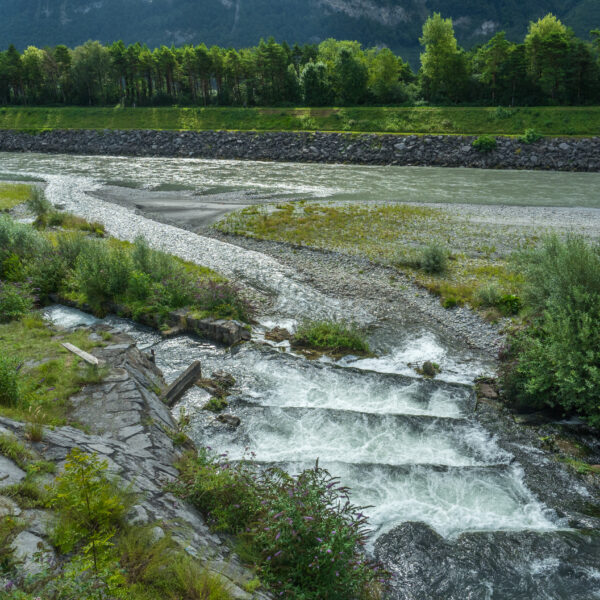 Vilterser-Wangser-Kanal: Fluss mit Kaskaden und Uferbefestigung vor bewaldetem Hintergrund.