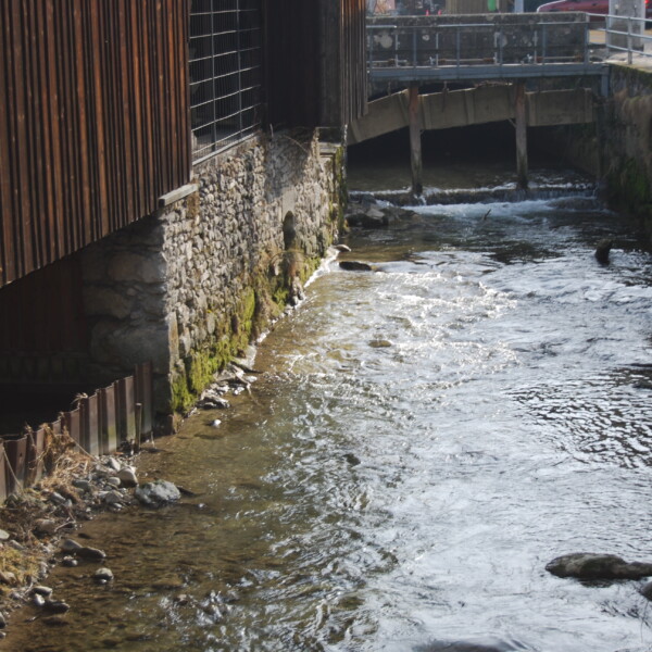 Fließende Wyna unter einer Brücke mit Steinmauern und Holzstrukturen.