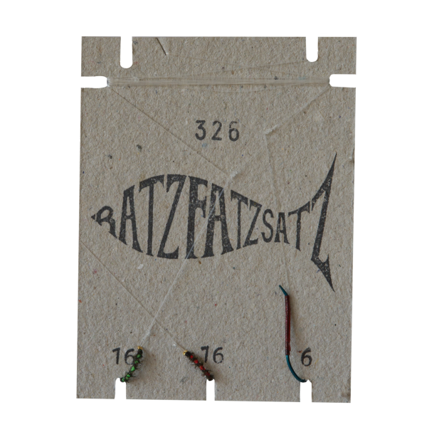 Auf einem braunen Karton mit der Aufschrift „RatzFatzSatz 326 (Grün & Rot)“ sind eine schwarze Fischabbildung, die Zahlen 16 und 6 in Grün und Rot sowie zwei kleine Angelfliegen am unteren Rand angebracht.