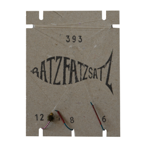 Auf einem Papphalter „RatzFatzSatz 393 (Weiss & Rot)“ in Fischform sind Angelfliegen in den Größen 12, 8 und 6 ausgestellt, die jeweils mit Fäden der Marken Weiss und Rot gebunden sind.