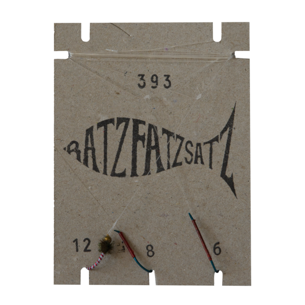 Auf einem Papphalter „RatzFatzSatz 393 (Weiss & Rot)“ in Fischform sind Angelfliegen in den Größen 12, 8 und 6 ausgestellt, die jeweils mit Fäden der Marken Weiss und Rot gebunden sind.