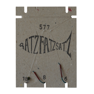 Der RatzFatzSatz 577 (Weiss & Schwarz) ist ein fischförmiger Papphalter in der Farbe Weiss mit den Zahlen „577“, „18“, „8“ und „6“, an dessen Unterseite drei Angelhaken angebracht sind.