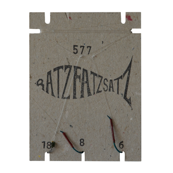 Der RatzFatzSatz 577 (Weiss & Schwarz) ist ein fischförmiger Papphalter in der Farbe Weiss mit den Zahlen „577“, „18“, „8“ und „6“, an dessen Unterseite drei Angelhaken angebracht sind.