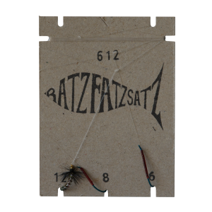 Ein fischförmiger Papphalter mit der Aufschrift „RatzFatzSatz 612 (Weiss)“ trägt darunter die Nummern 12, 8 und 6 und an drei Schnüren sind Weiss-Angelfliegen befestigt.