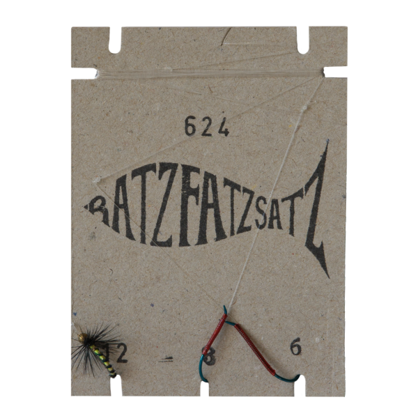 Ein Stück Pappe mit der Aufschrift „RatzFatzSatz 624 (Gelb)“ zeigt ein schwarzes Fischmotiv, zwei Angelhaken an Schnüren und einen Fliegenköder mit einem Hauch von Gelb bei der Zahl „2“ in der unteren linken Ecke.