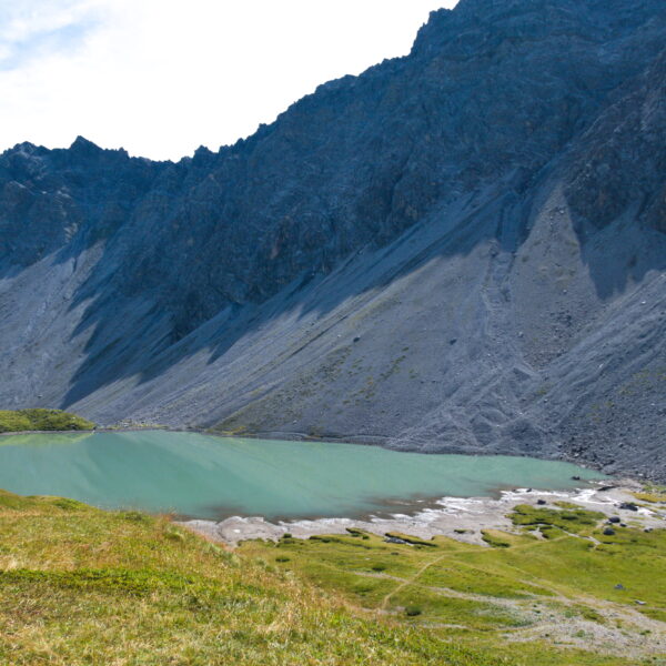 Älplisee: Türkisfarbener Bergsee in Graubünden, umgeben von grünen Wiesen und steilen Felswänden.