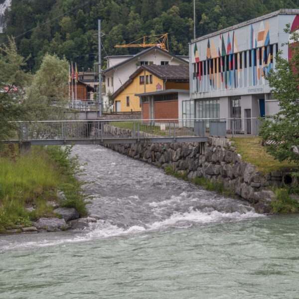 Fluss in Alpbach (Meiringen) unter einer Brücke mit Gebäuden im Hintergrund.