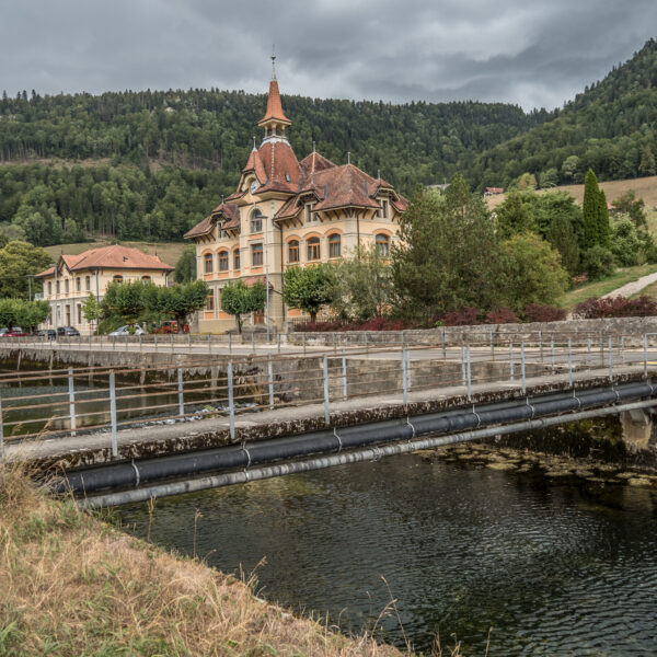 Areuse: Brücke über den Fluss mit historischem Gebäude im Hintergrund.