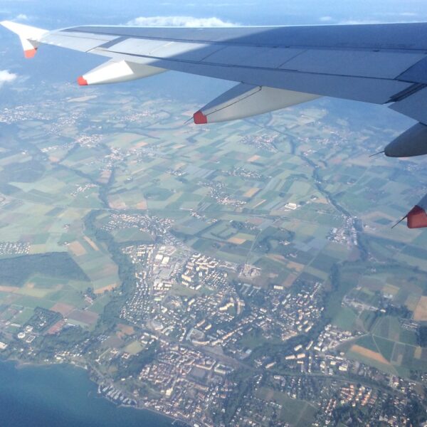 Flugzeugflügel über Asse, Schweiz, mit Feldern und Stadtansicht.