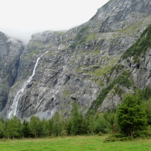 Balmhornbach: Wasserfall an steiler Felswand, umgeben von grünen Bäumen und Wiesen.