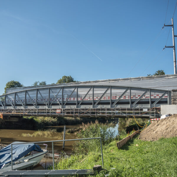 Broye-Brücke im Bau mit Abdeckung und Uferböschung. Flusslandschaft mit Booten.